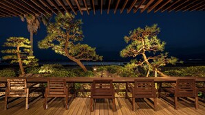 A wooden deck with a row of chairs and a pergola overhead.