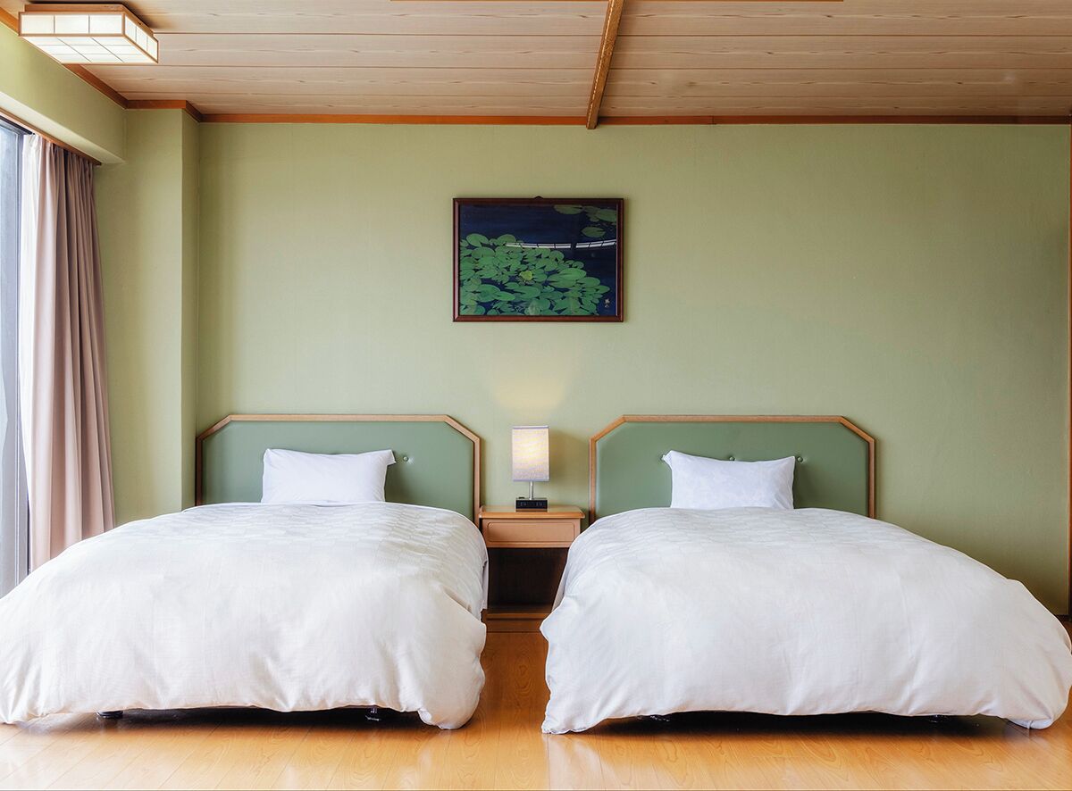 Una habitación con dos camas, una mesita de noche con lámpara, un cuadro en la pared y suelo de madera.