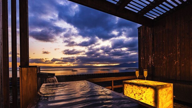 A hot tub with a wooden deck and a view of the ocean and sunset.
