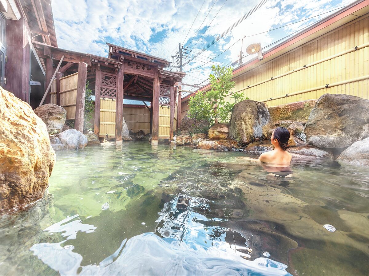 A traditional Japanese onsen with clear water, wooden structures, and large rocks.