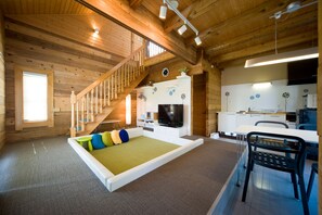 L’intérieur chaleureux d’un chalet en bois comprend un escalier en bois, un téléviseur à écran plat, un coin repas et une cuisine.