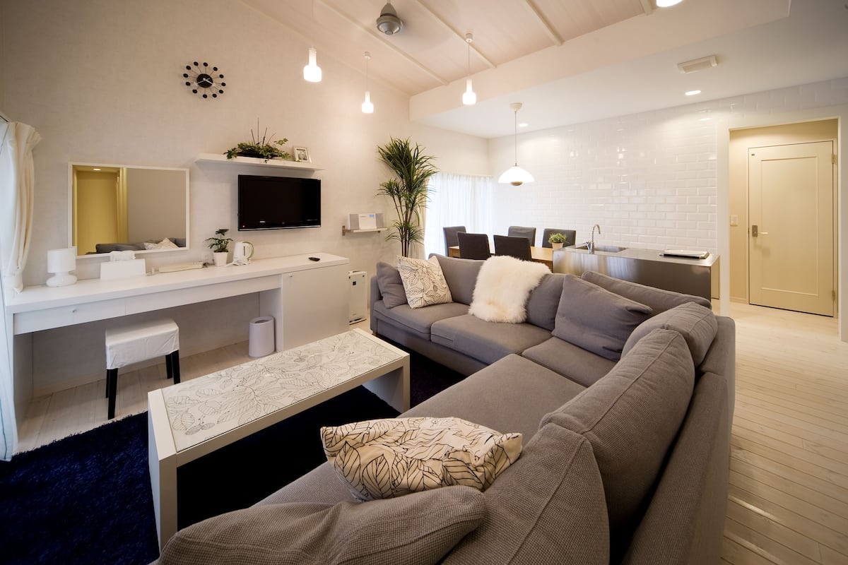 A modern living room with a sofa, coffee table, and a TV. There is a dining area with chairs and a table.