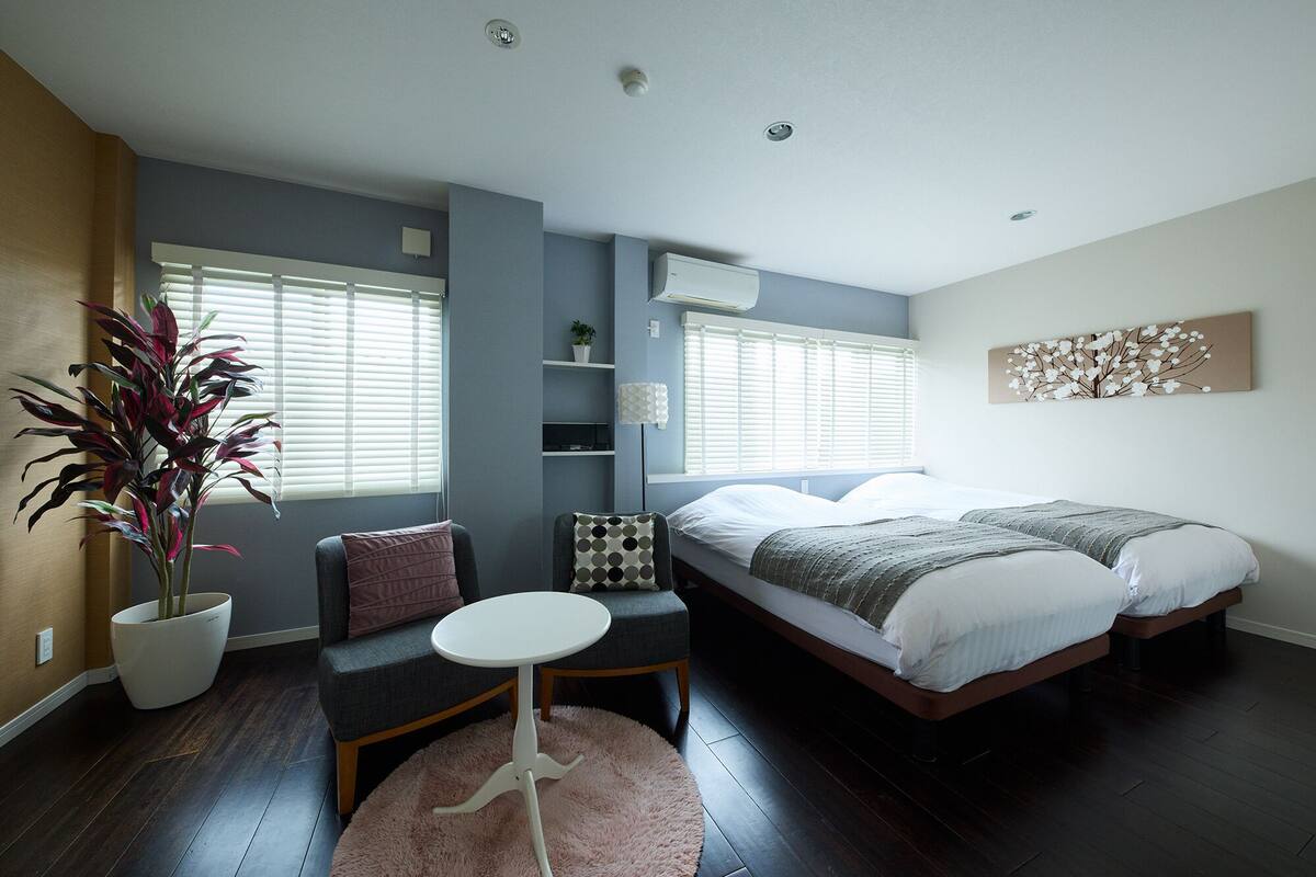 A modern bedroom with a bed, a small table, a chair, and a potted plant.