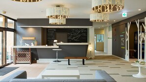 Een moderne hotellobby met een receptiebalie, een zithoek en een koffieapparaat.