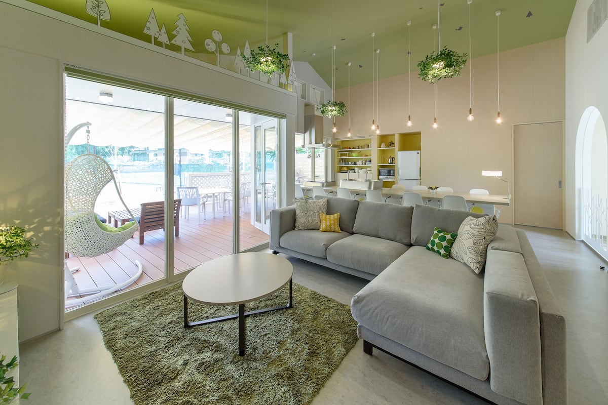 A modern living room with a grey sofa, a round coffee table, and a hanging chair. There is a large window with a view of the outdoors.