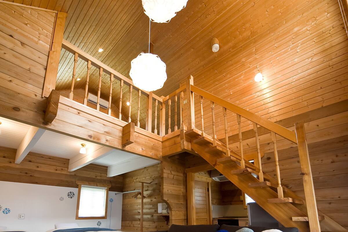 A wooden cabin interior with a loft bedroom, a sofa, a white coffee table, and a staircase.