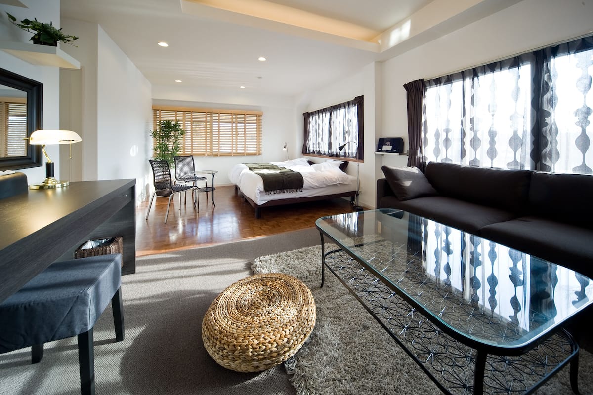 A modern living room with a glass coffee table, a sofa, a bench, and a wicker ottoman.