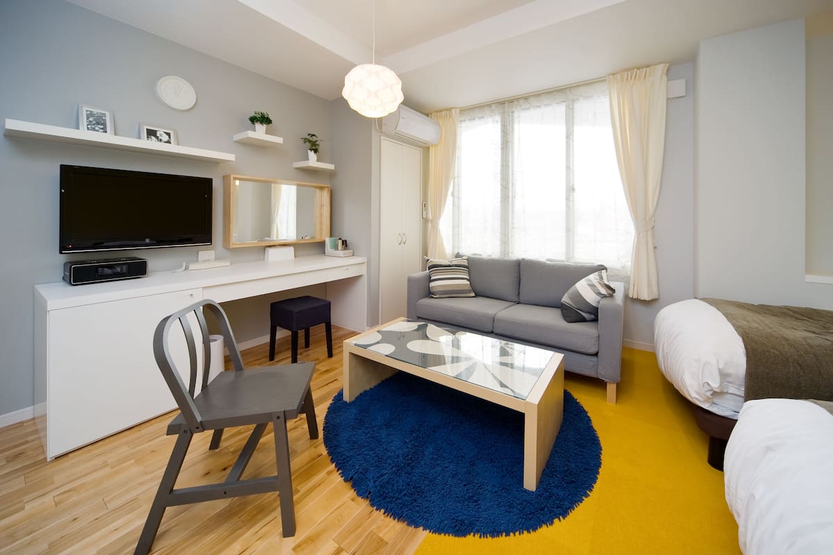 A modern living room with a flat-screen TV, a sofa, a coffee table, and a dining area with a chair.