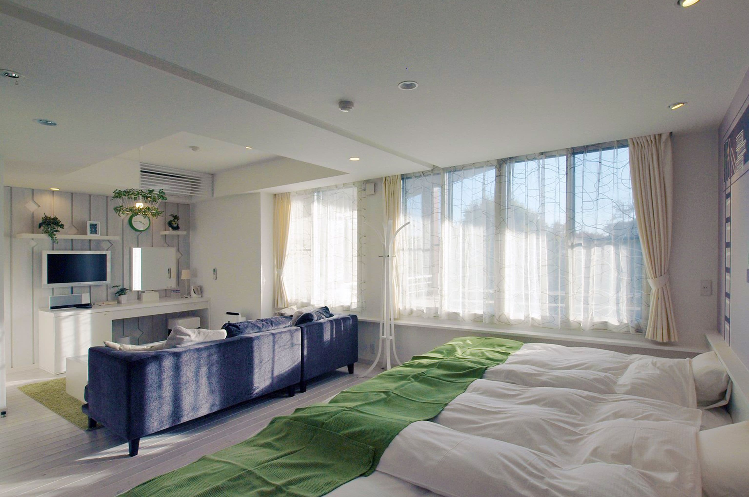 Un dormitorio moderno con una cama grande, un sofá, un televisor y una ventana con cortinas.