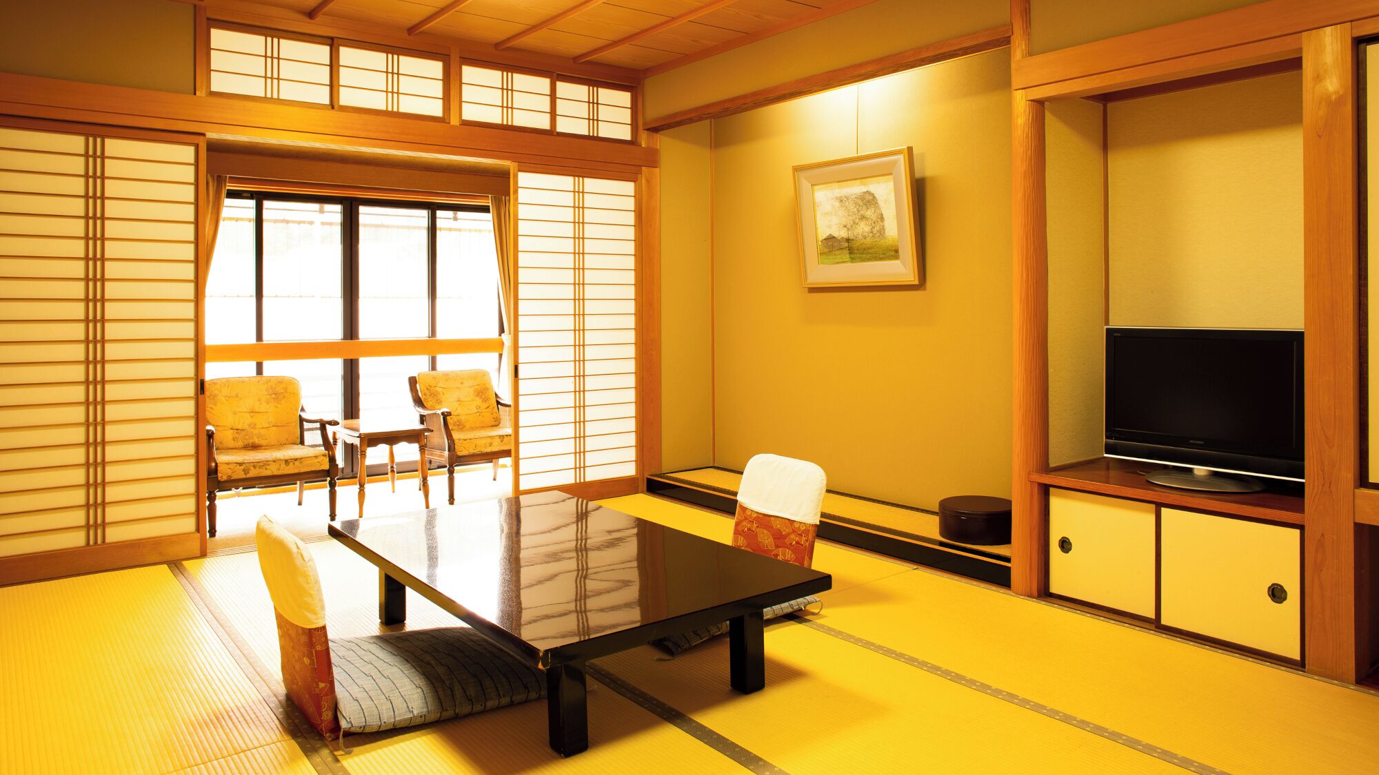 Een traditionele Japanse kamer met tatami vloerbedekking, een lage tafel, twee stoelen, een televisie en schuifdeuren.