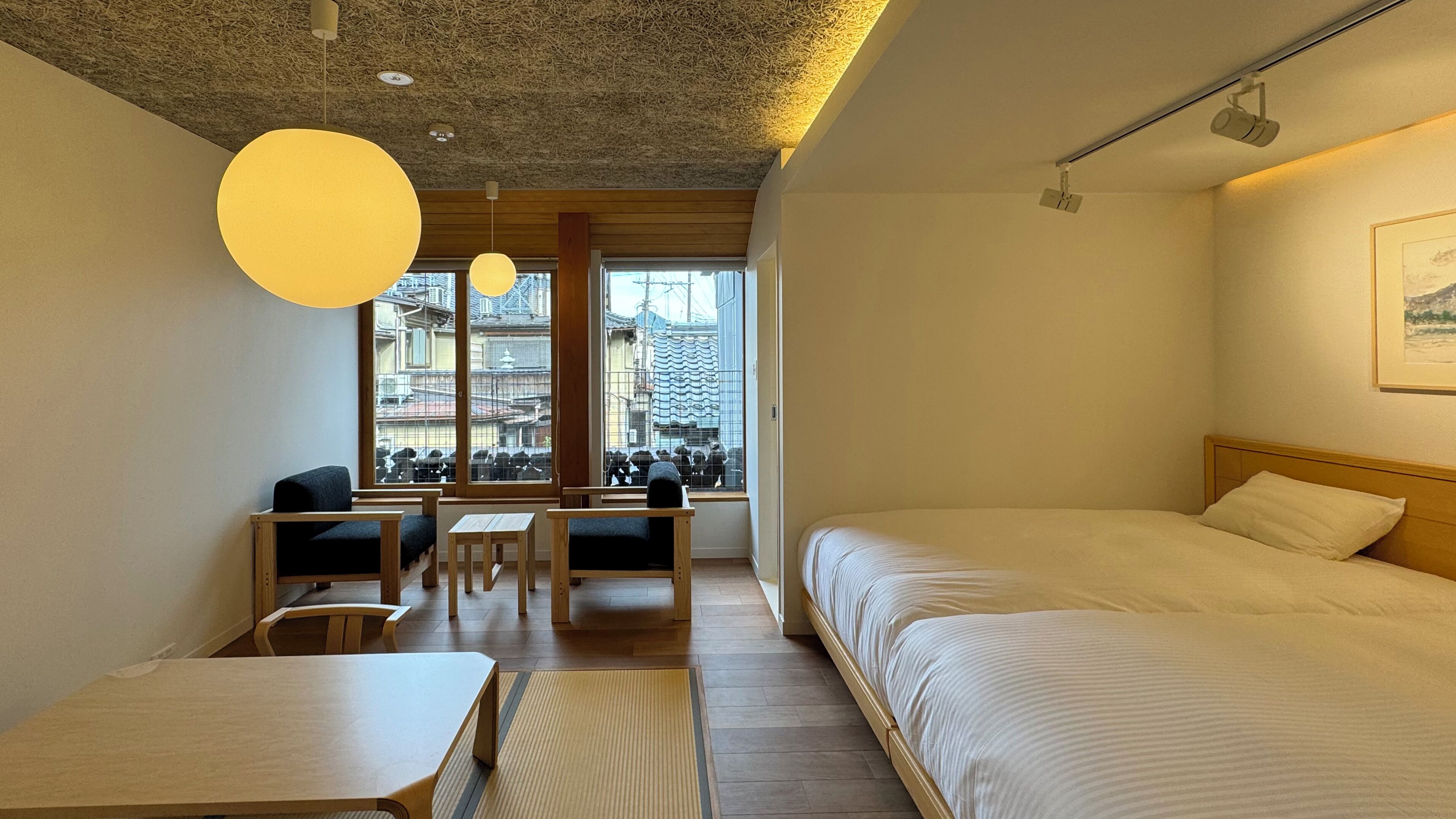Een hotelkamer met een bed, een bureau, twee stoelen, een raam met uitzicht op gebouwen, en een plafond met een structuur.