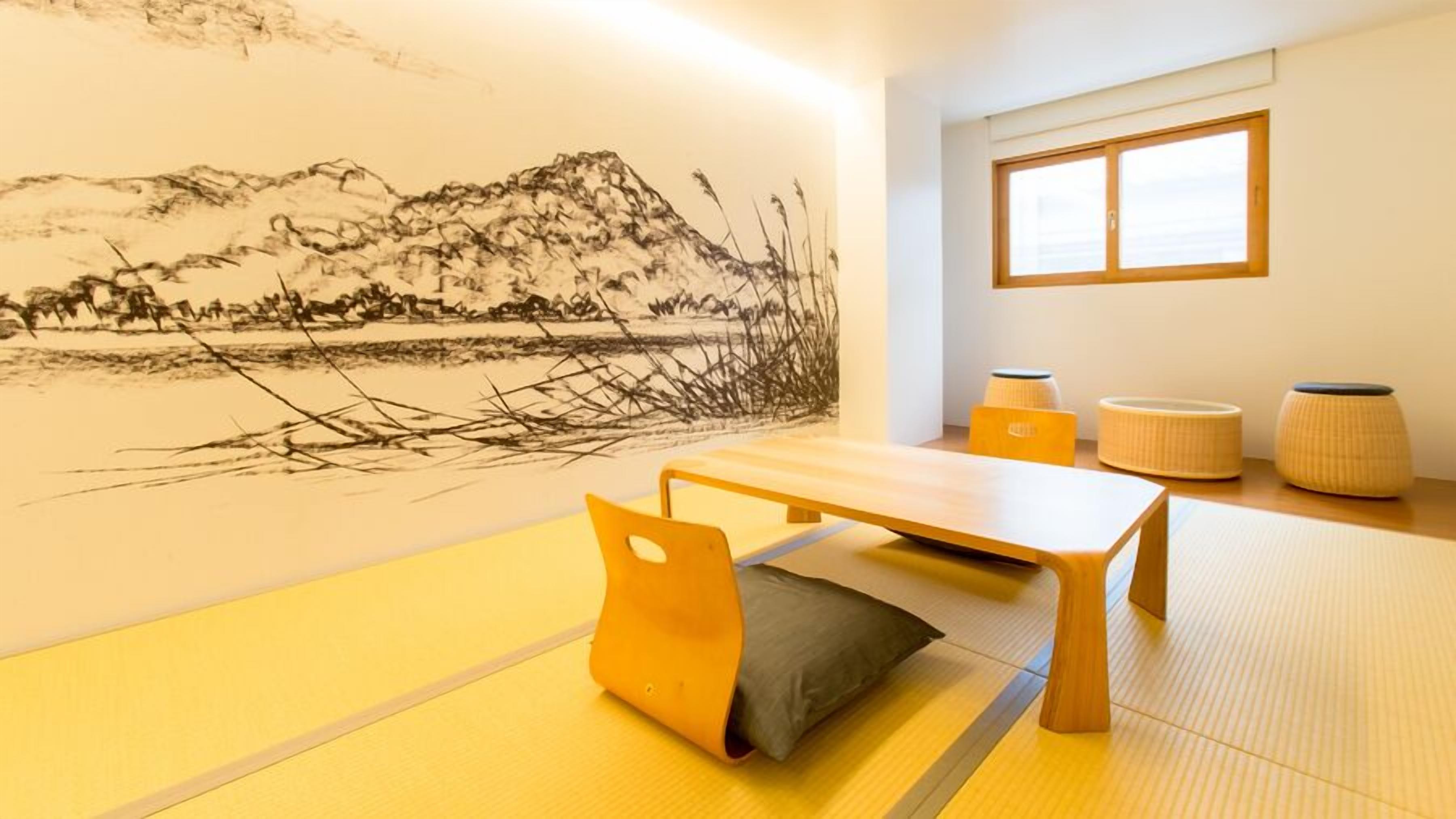 Una habitación con tatami, una mesa baja, cojines y una pintura mural.