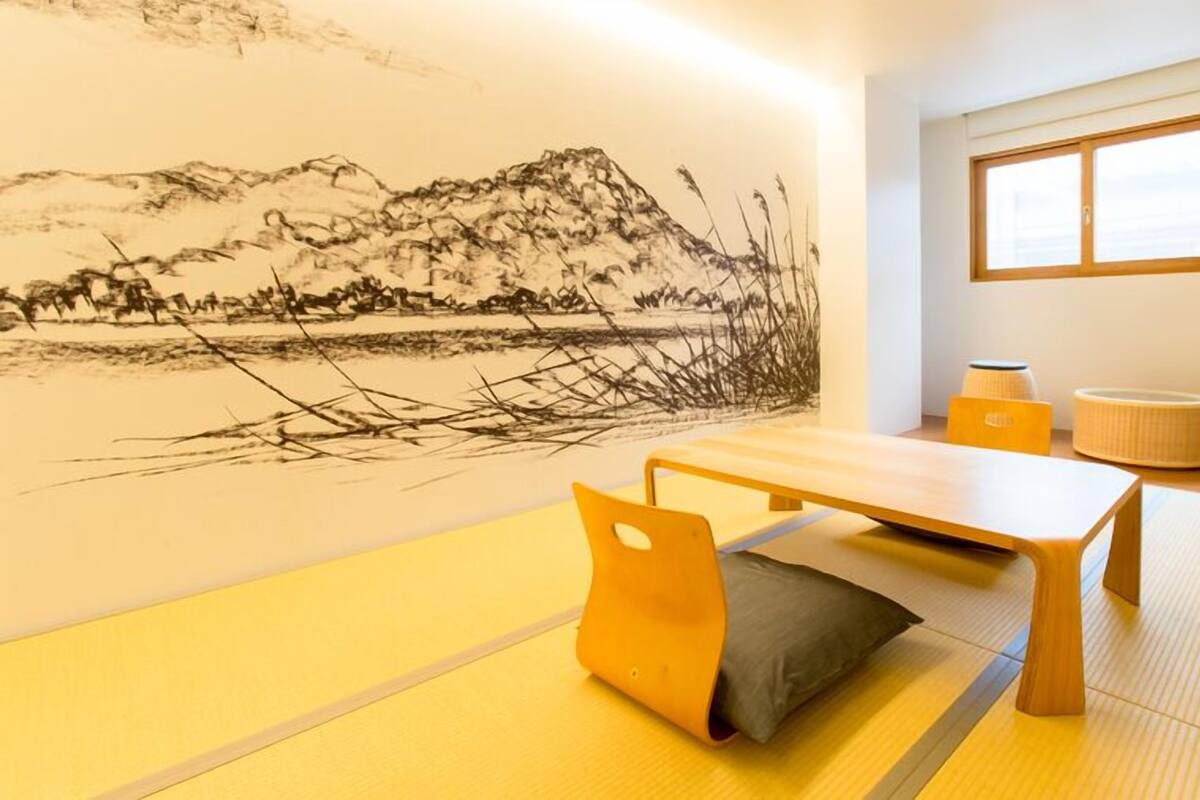 Een kamer met tatami matten, een lage tafel, kussens en een muurschildering.