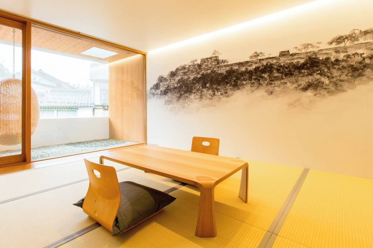 Een traditionele Japanse kamer met tatami vloerbedekking, een lage tafel en een schuifdeur die uitkomt op een uitzicht over traditionele gebouwen.