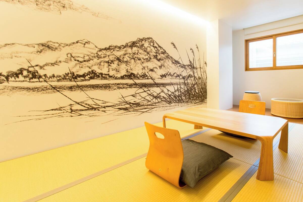Een kamer met tatami matten, een lage tafel, kussens en een wanddecoratie.