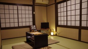 Une pièce de style japonais traditionnel, avec un sol recouvert de tatamis, une petite table basse avec un coussin, un téléviseur et une lampe de chevet.