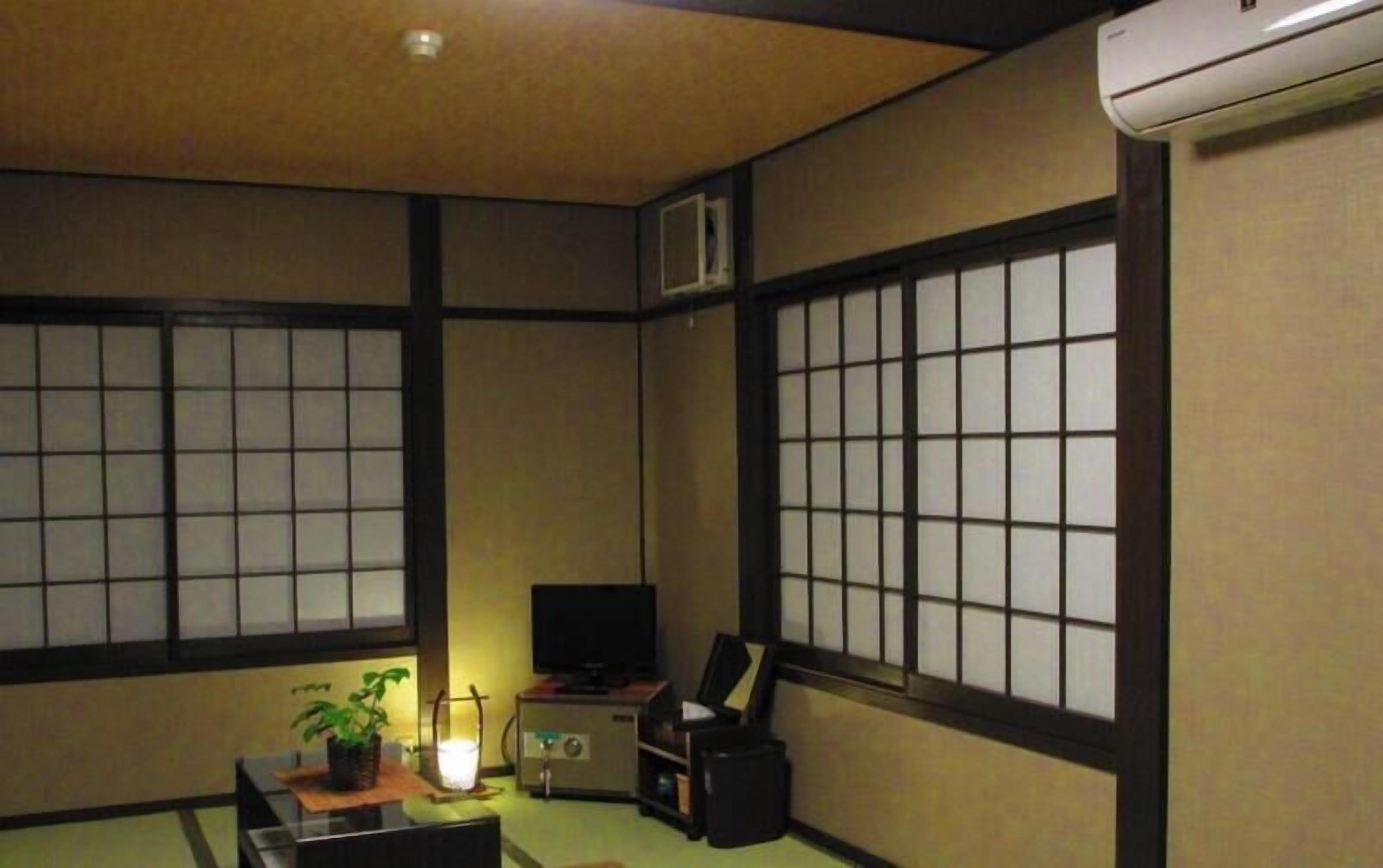 A traditional Japanese room with tatami flooring, shoji screens, a television, a desk with a computer, and a small plant.