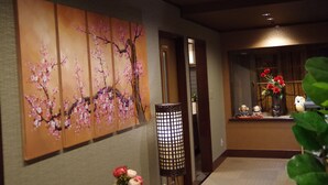 Un couloir orné d’un grand tableau représentant des motifs floraux, d’un lampadaire et d’une fenêtre agrémentée d’objets décoratifs.