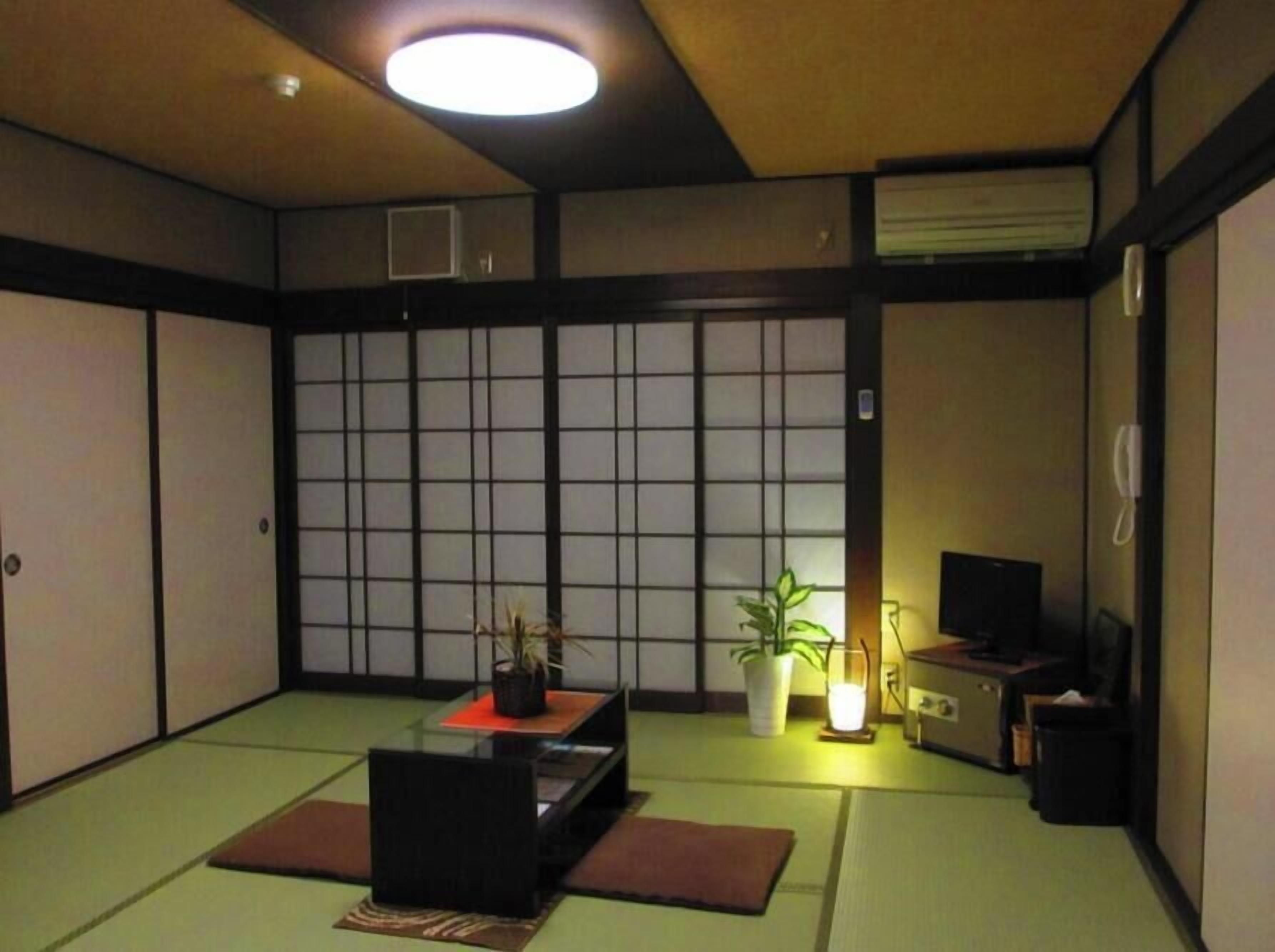 A traditional Japanese room with tatami flooring, a low table with a plant, a television, and a heater.