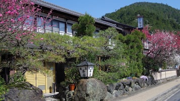 A traditional Japanese building with a wooden exterior, large rock in front, and cherry blossoms in the background.