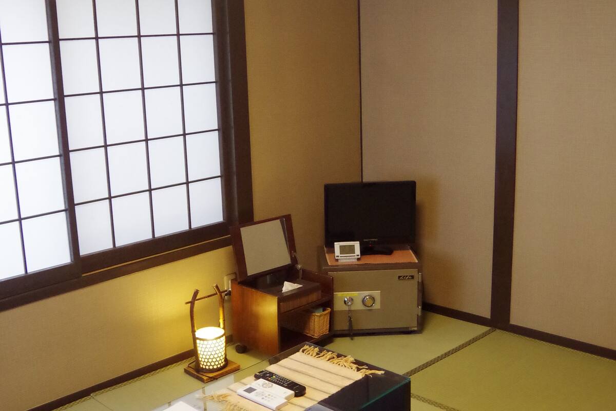 Ein traditioneller japanischer Raum mit Tatami-Böden, einem niedrigen Tisch mit Unterlagen, einem Fernseher und einem Laternen.