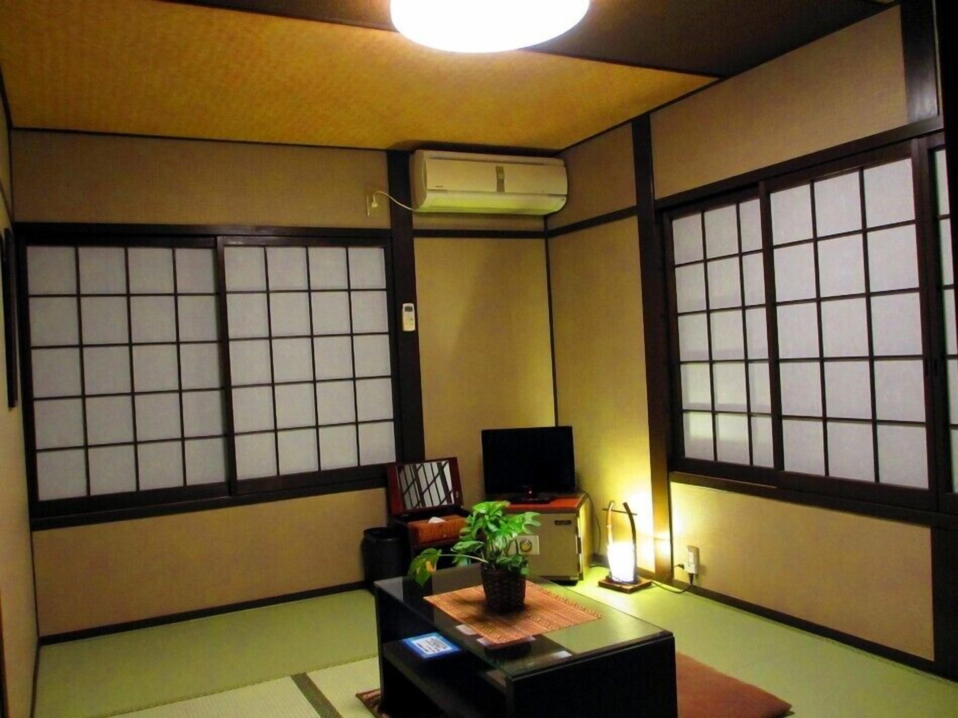 A traditional Japanese room with tatami flooring, shoji screens, a television, a heater, and a small plant.