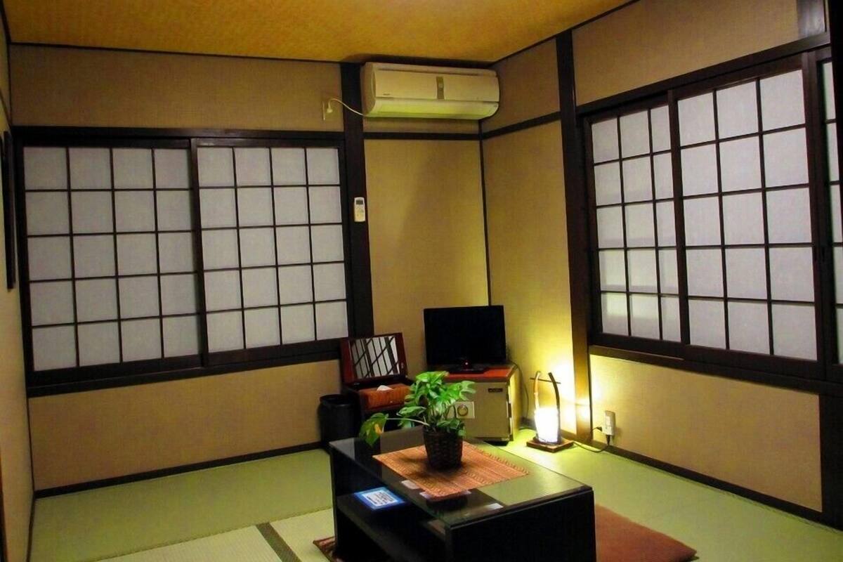 Ein traditioneller japanischer Raum mit Tatami-Böden, Shoji-Bildschirmen, einem Fernseher, einer Heizung und einer kleinen Pflanze.