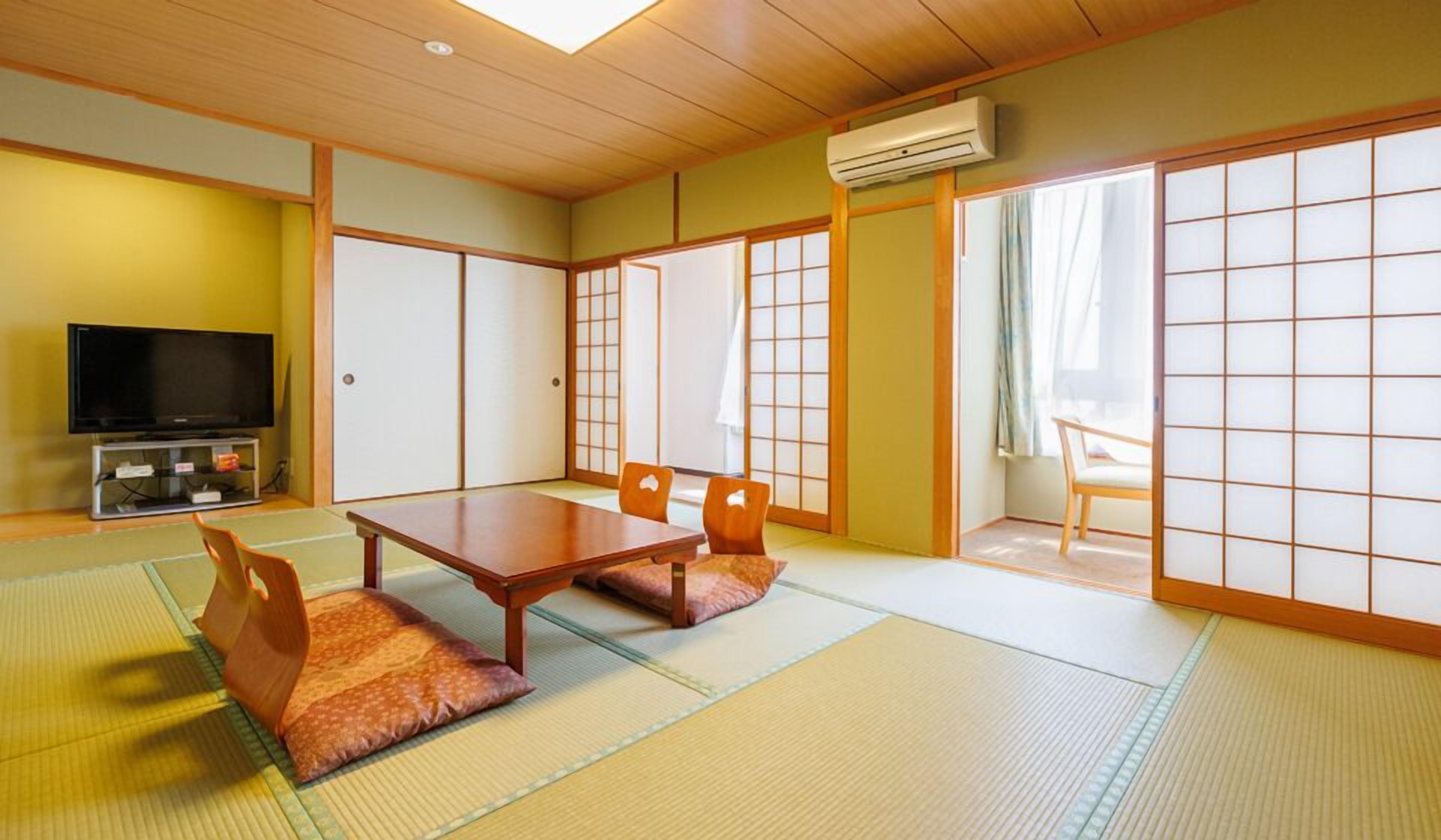 A traditional Japanese room with tatami flooring, a low table with cushions, sliding doors, and a television.