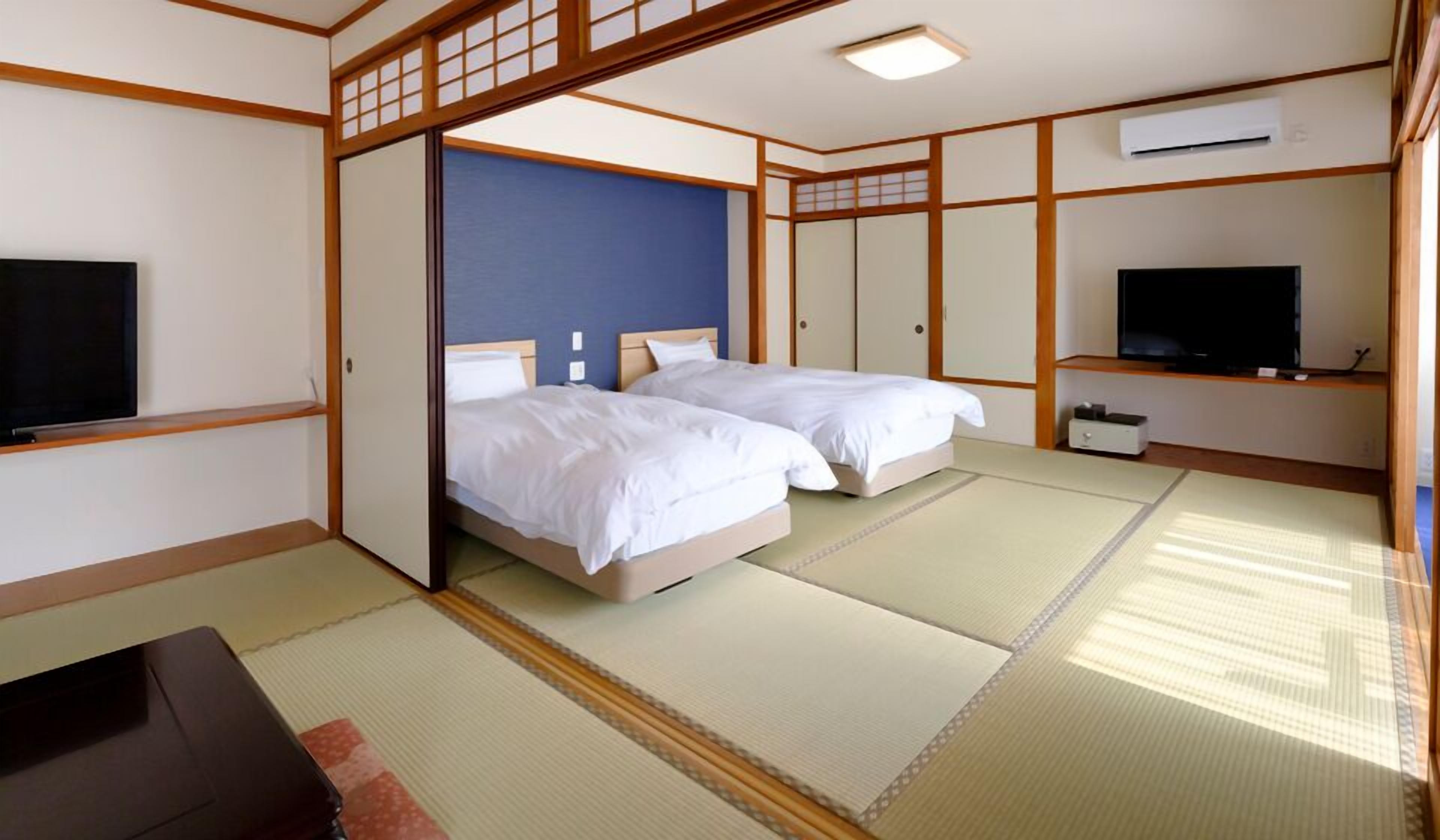 A traditional Japanese-style room with tatami flooring, two beds, a television, and a sliding door.