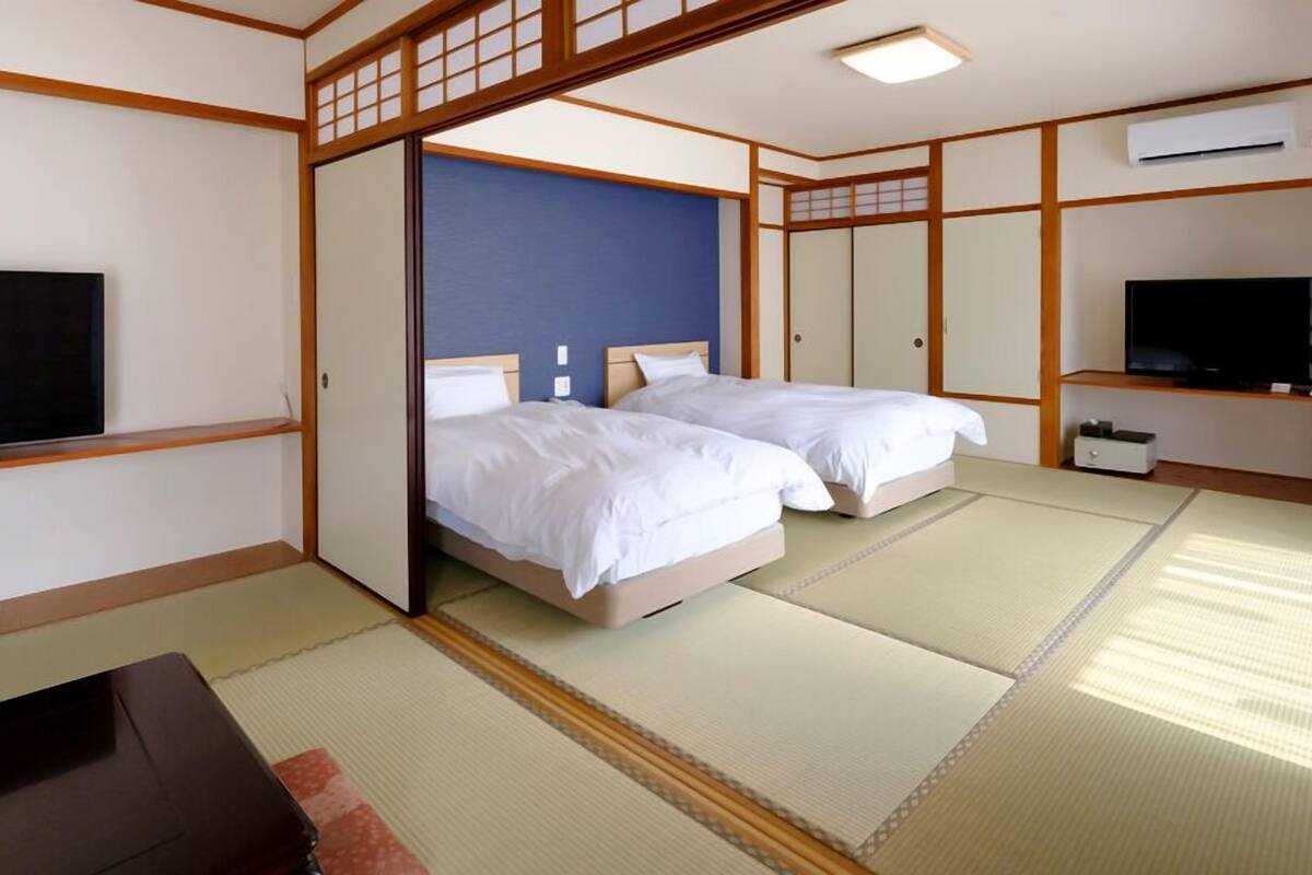A traditional Japanese-style room with tatami flooring, two beds, a television, and a sliding door.