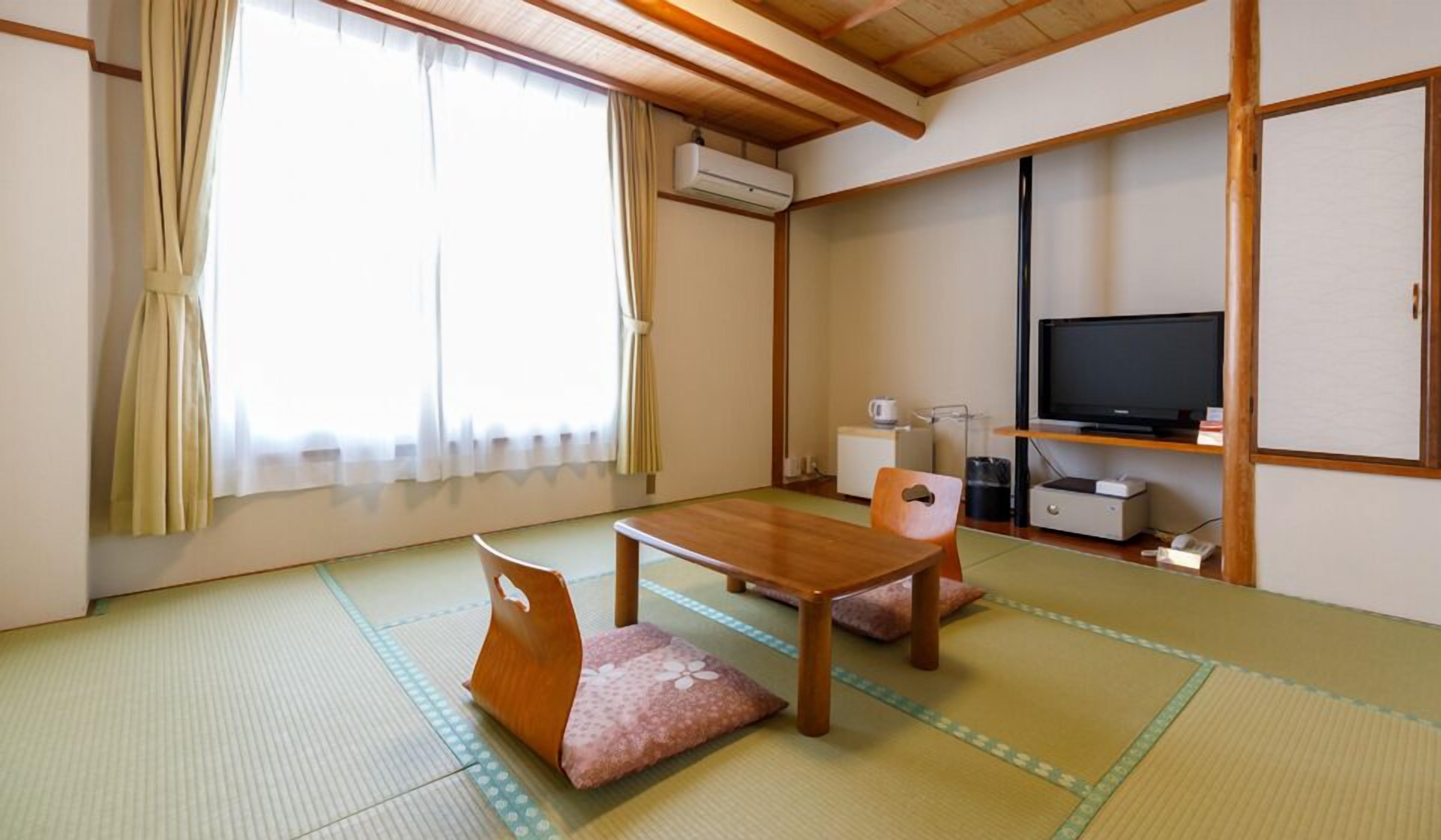 Une pièce de style japonais traditionnel, avec un sol recouvert de tatamis, une table en bois, un téléviseur et un futon servant de lit.