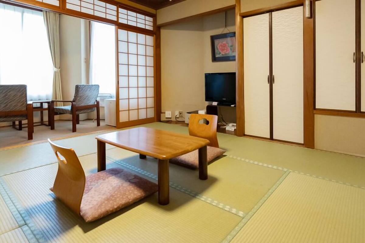 A traditional Japanese room with tatami flooring, a low table, chairs, a television, and sliding doors.
