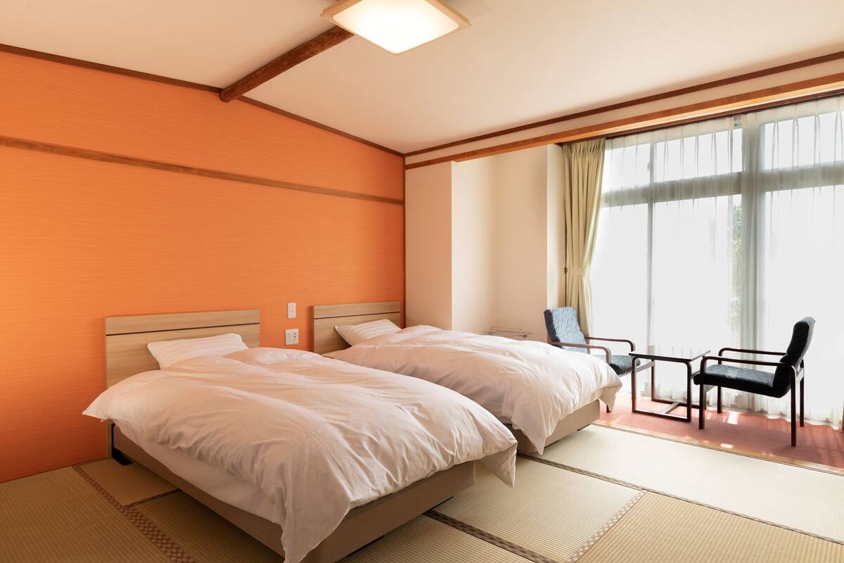 A hotel room with two beds, a sitting area with chairs, and a large window with curtains.