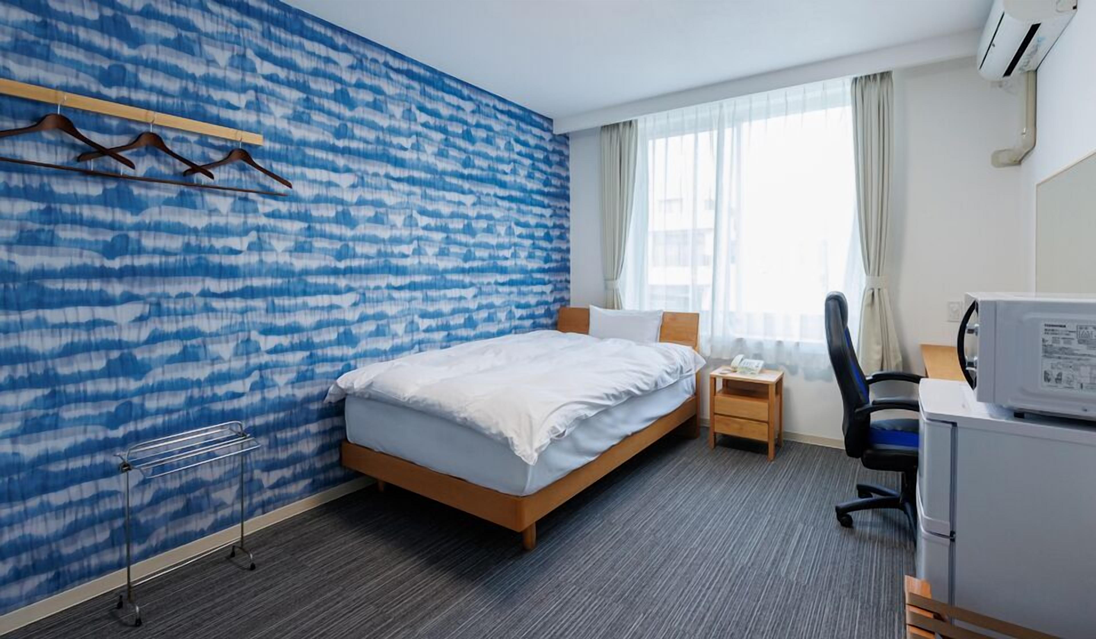 Une chambre d’hôtel équipée d’un lit, d’un bureau, d’une chaise, d’une petite table et d’un climatiseur fixé au mur.