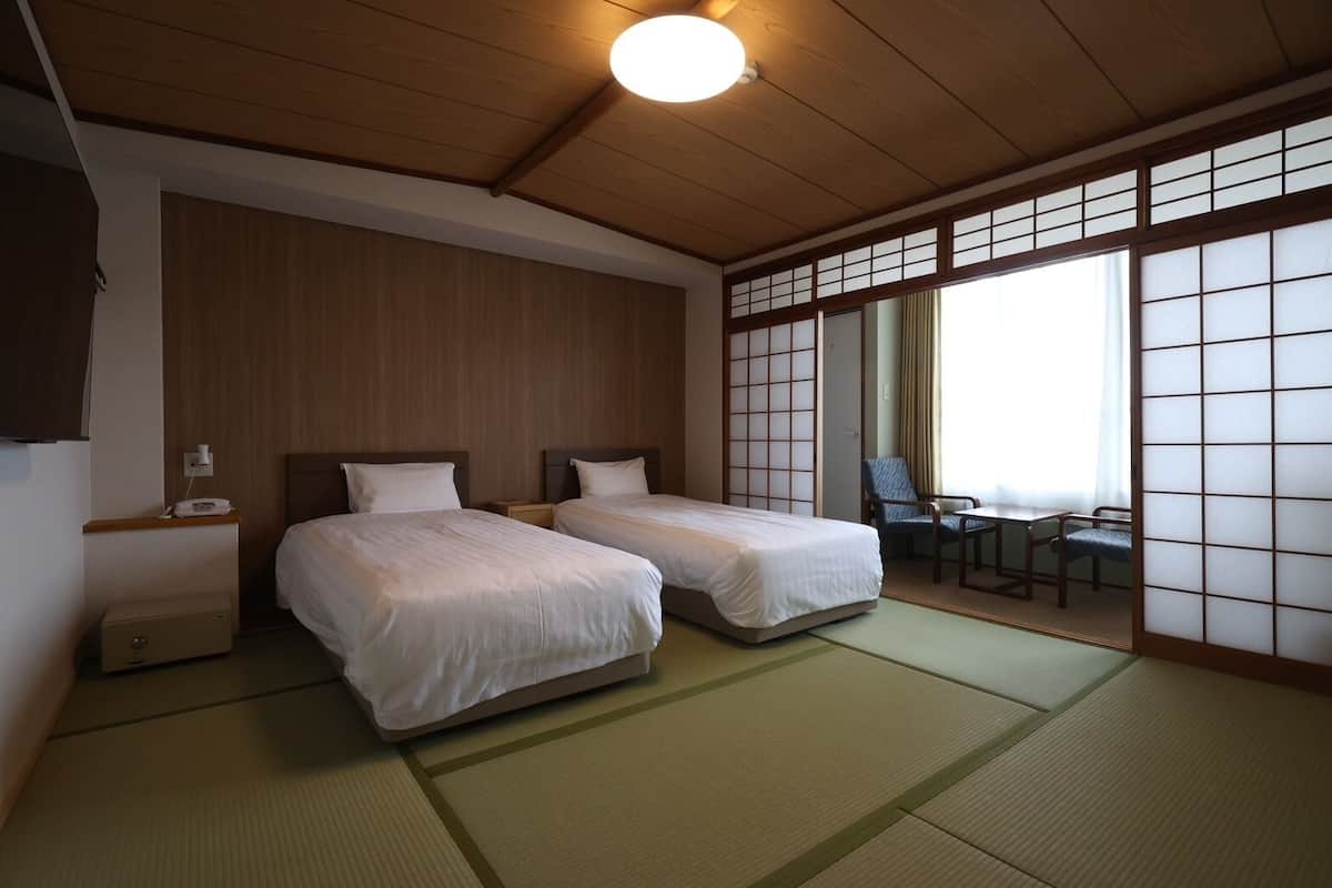 A traditional Japanese room with tatami flooring, two beds, a desk with chairs, and a sliding shoji screen.
