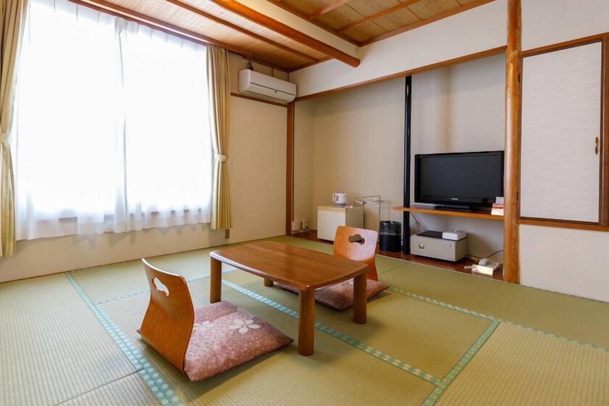 A traditional Japanese room with tatami flooring, a low wooden table, a television, and a futon bed.