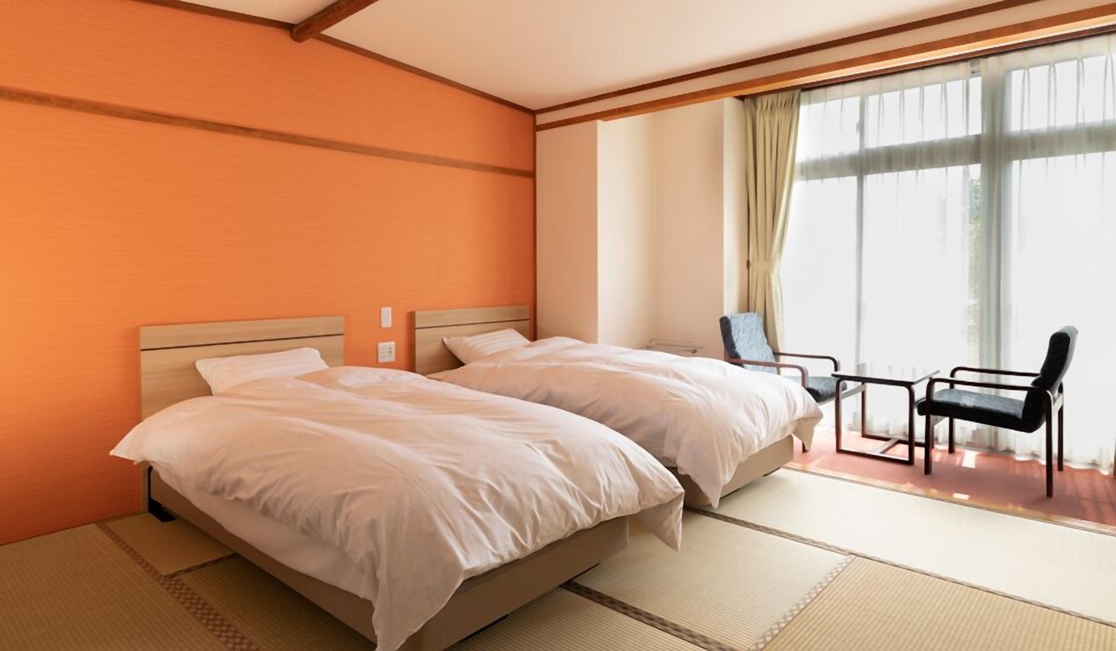Une chambre d’hôtel avec deux lits, une chaise et une grande fenêtre avec des rideaux.