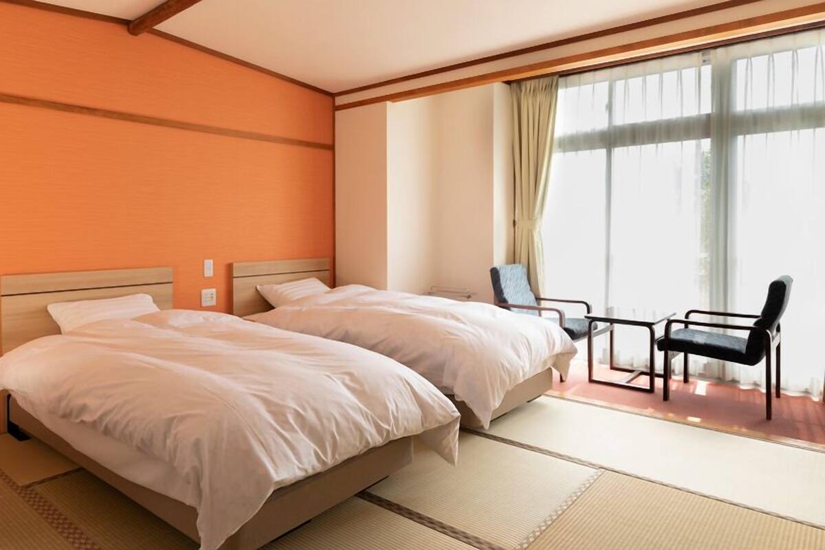 A hotel room with two beds, a chair, and a large window with curtains.