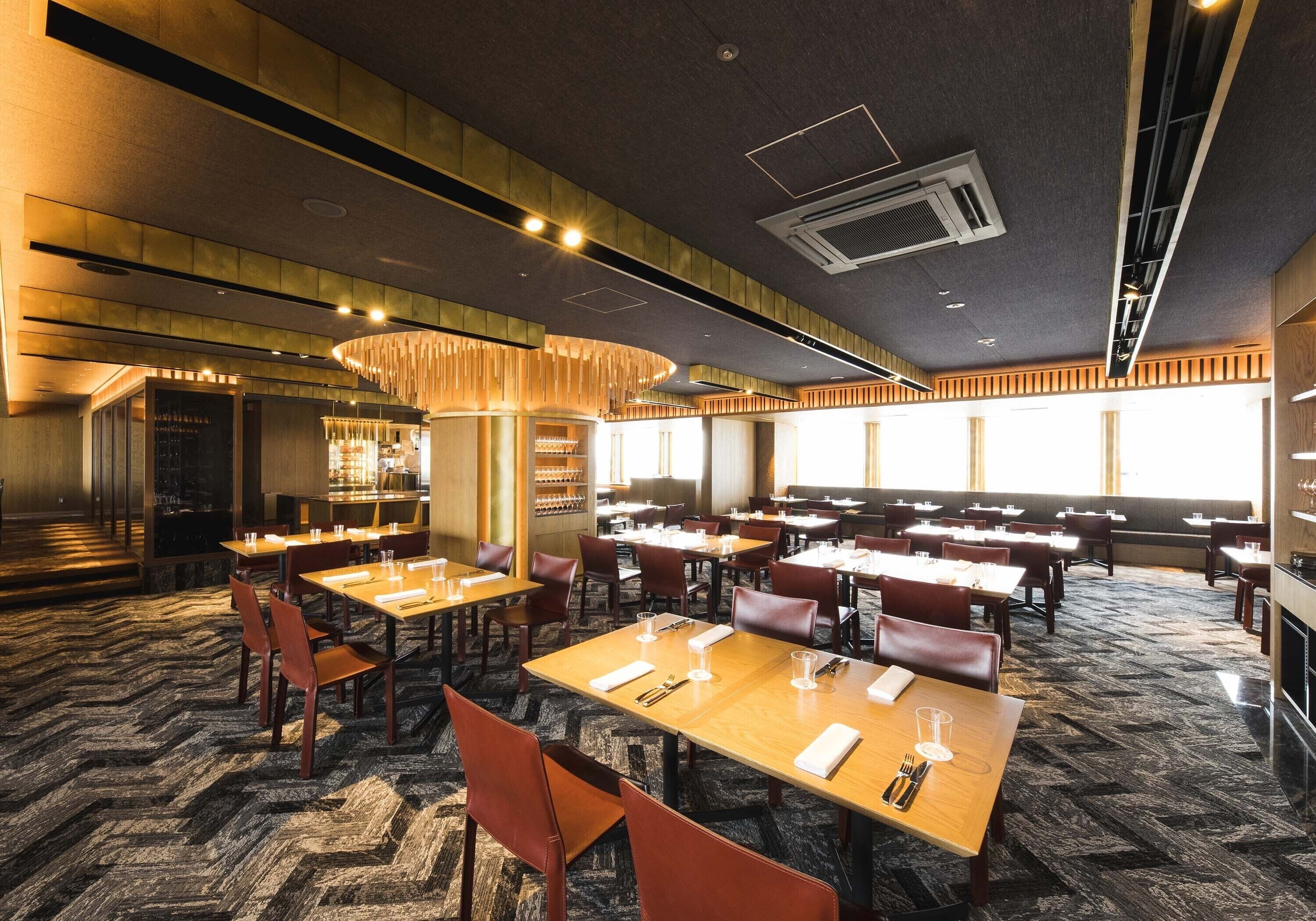 A spacious restaurant with multiple dining tables and booths, a patterned carpet, and a modern ceiling design.