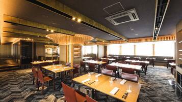 A spacious restaurant with multiple dining tables and booths, a patterned carpet, and a modern ceiling design.