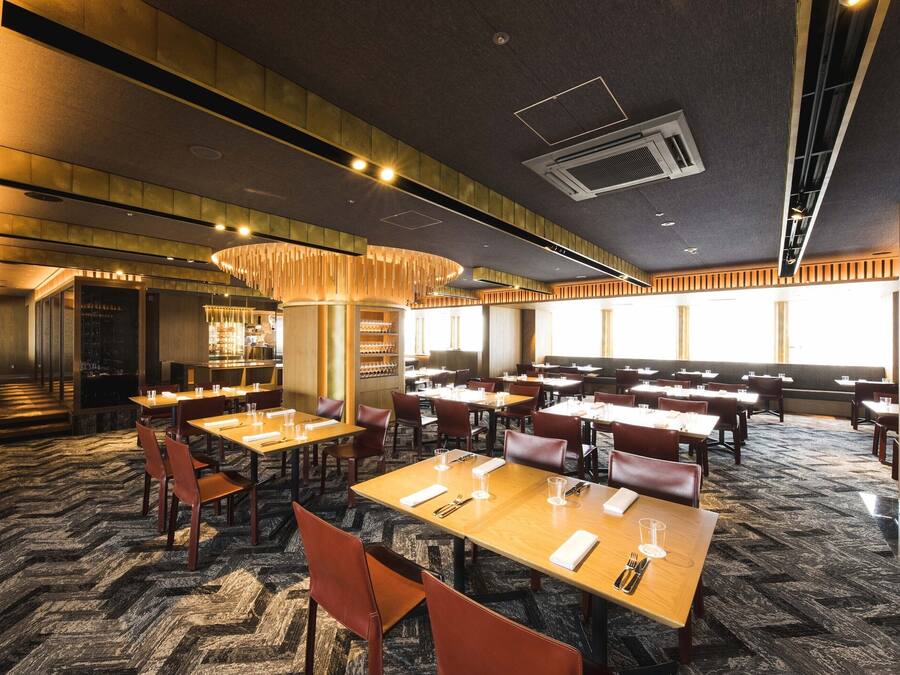 A spacious restaurant with multiple dining tables and booths, a patterned carpet, and a modern ceiling design.
