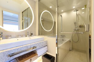 Un baño moderno con ducha de vidrio, tocador de mármol y un espejo grande con iluminación circular.