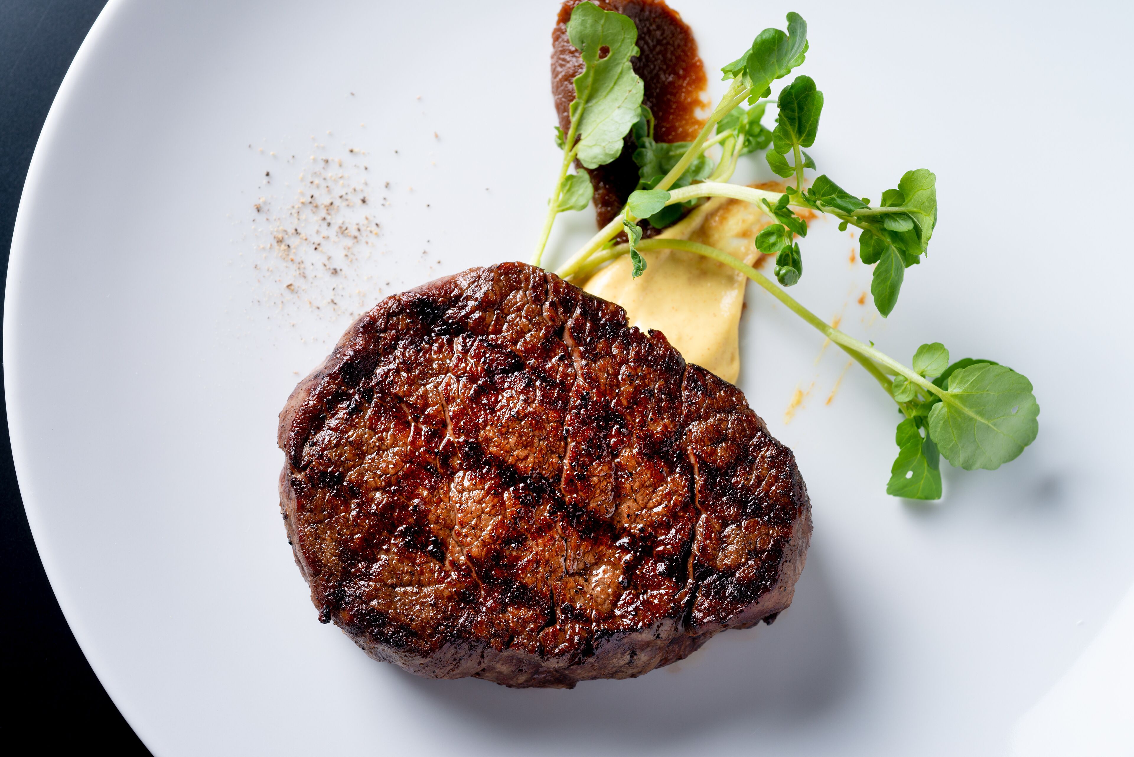 A steak with a side of greens and a sauce on a plate.