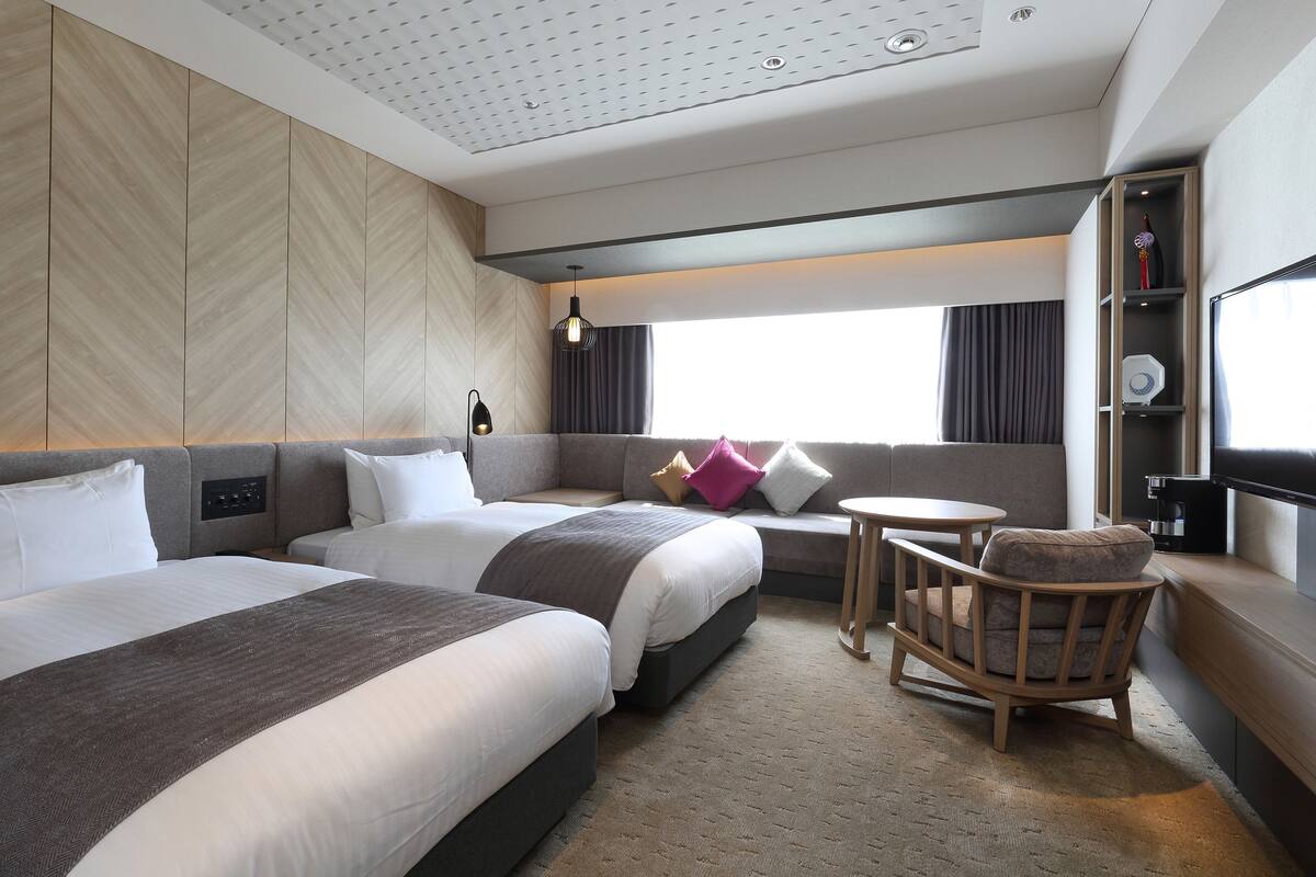 A hotel room with two beds, a sofa, a small table, and a TV.