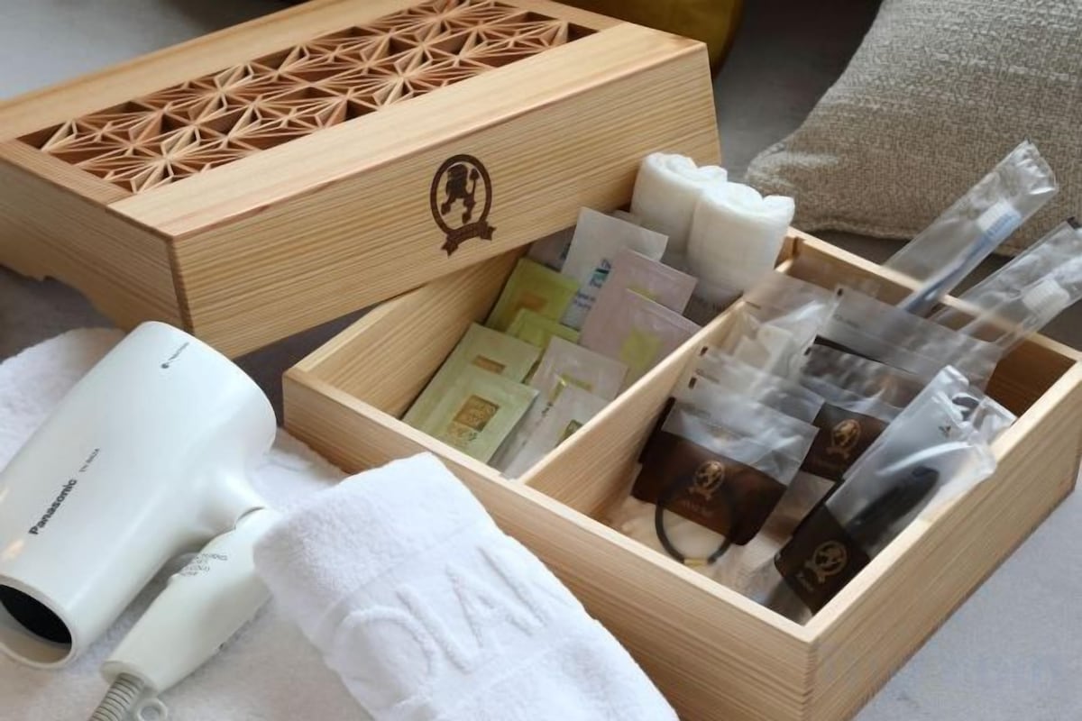 Una caja de madera con distintos artículos de aseo personal y un secador de pelo blanco sobre una toalla.