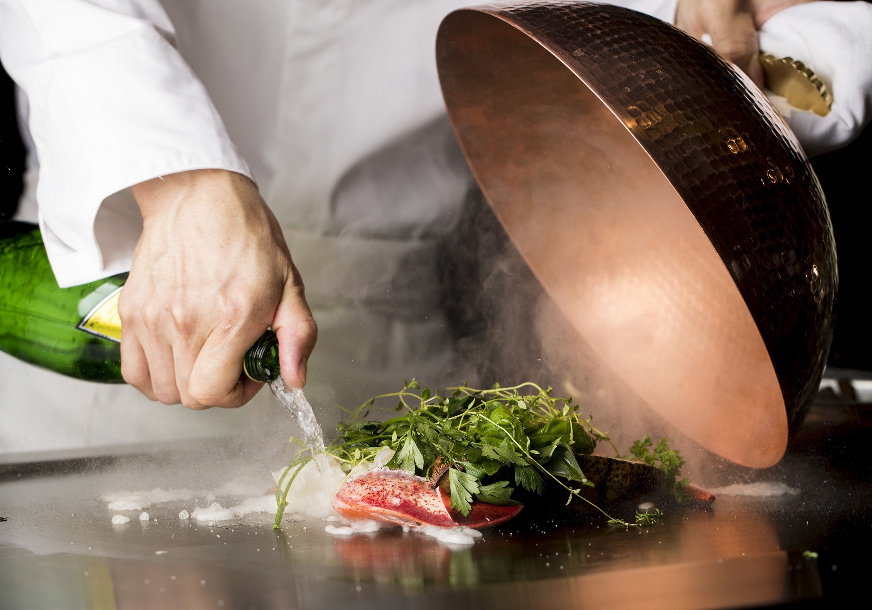 Un chef sirviendo agua sobre un plato con carne y hierbas.