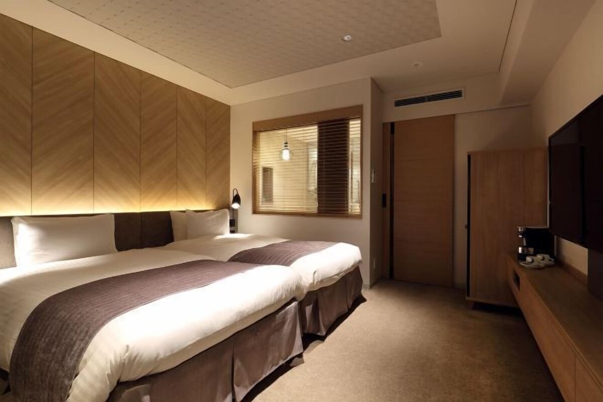 Un dormitorio con dos camas, un armario, un televisor y una ventana con persianas.