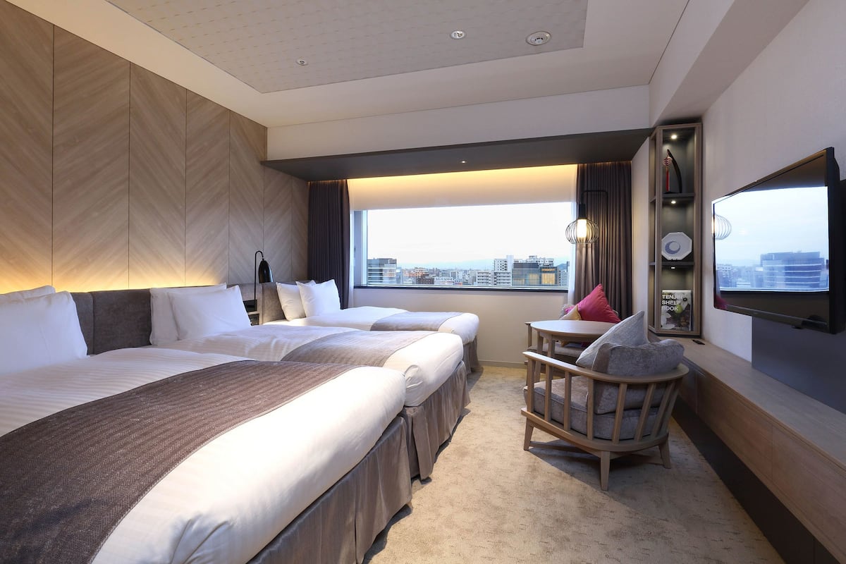 A hotel room with two beds, a seating area, a TV, and a city view.