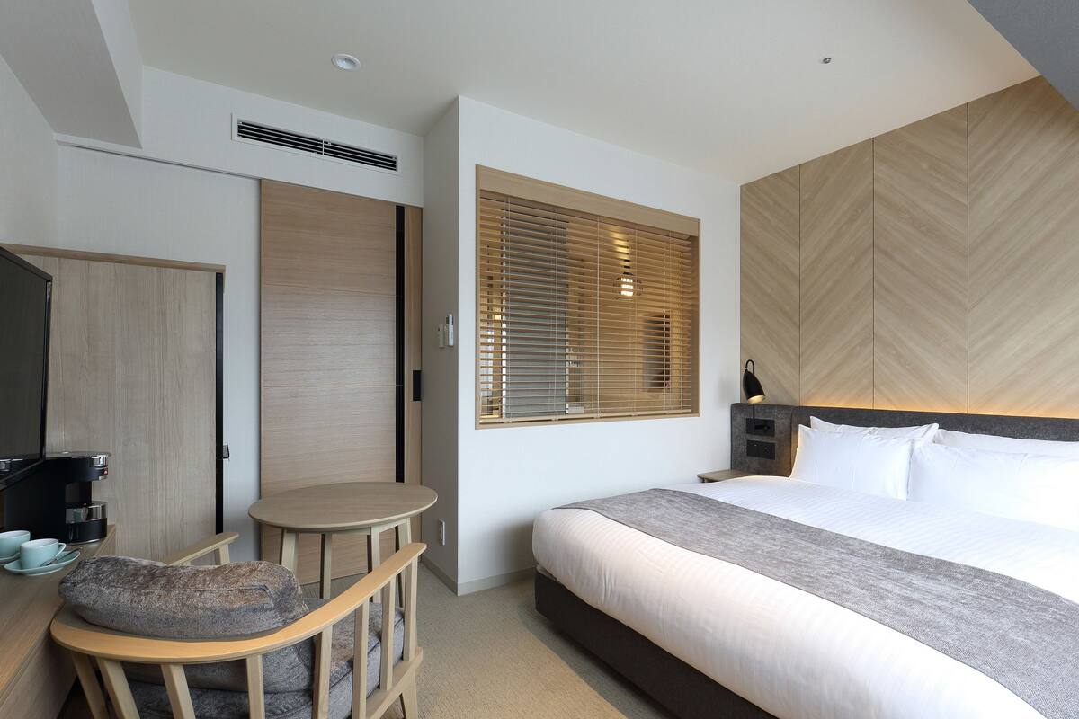 A modern hotel room with a large bed, a small round table, a sofa, and a coffee machine.