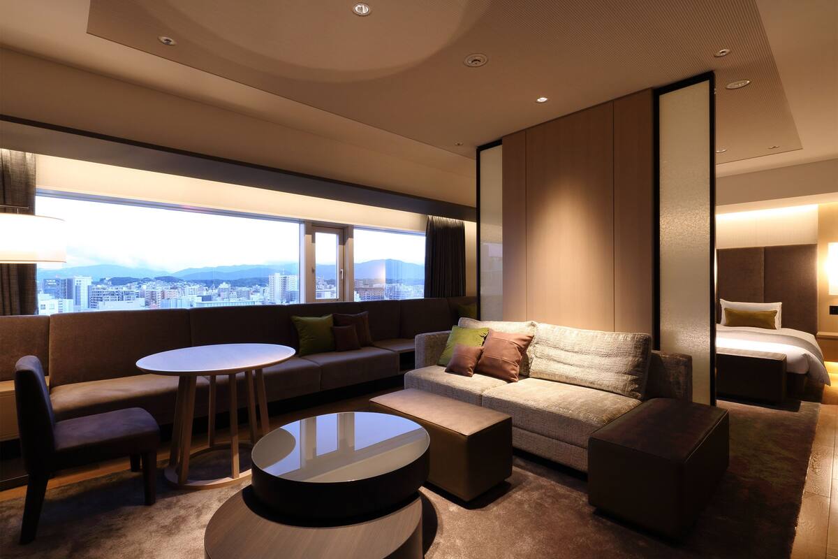 A modern hotel room with a city view, a sofa, a round table, and a bed.